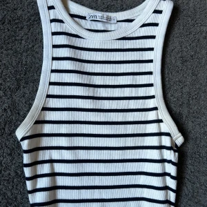 Randigt ribbat linne från Zara - Säljer en vit och svart ribbad linnetopp från Zara i storlek S. Toppen har smala svarta horisontella ränder, är ärmlös och har en croppad passform. Perfekt för varma dagar och enkel att matcha med jeans eller kjol. Endast använd ett fåtal gånger, säljer då den är för stor för mig.❤️