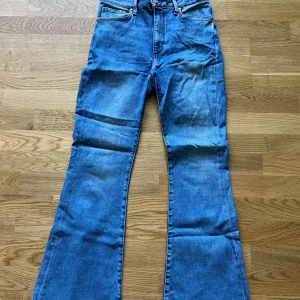 Blå bootcut jeans med hög midja - Snygga blå jeans med bootcut-modell och hög midja. Klassisk femficksdesign och dragkedja fram. Jeansen har en lätt utsvängd passform nertill och är tillverkade i ett mjukt denimtyg som ger en skön känsla.