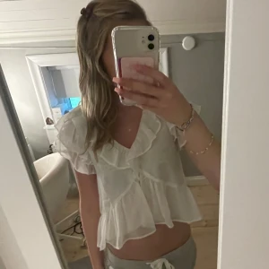 Vit volangblus från Nelly - Supersöt vit blus från Nelly med volanger längs ärmar, halsringning och nederkant. Blusen är lätt och luftig med korta ärmar och v-ringning, 