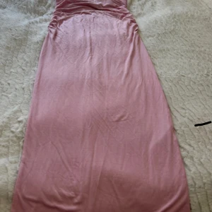 Rosa kjol från Gina Tricot - Supersnygg rosa kjol från Gina Tricot i mjukt material. Kjol har rynkade detaljer vid sidorna upptill och en rak, figurnära passform. Perfekt för dig som gillar en enkel men trendig look. Färgen är en ljus rosa ton.