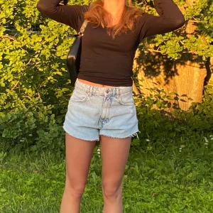 Ljusblå jeansshorts  - Säljer ett par ljusblå jeansshorts med fransig kant nertill. Snyggt slitna detaljer framtill för en avslappnad vibe. Perfekta för varma dagar och enkel att matcha med allt.