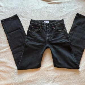 Svarta raka jeans från Zara - Snygga svarta jeans från Zara med raka ben och klassisk femficksdesign. Jeansen har hög midja och stängs med tre guldiga knappar framtill. Materialet är denim i bomull och passformen är normal. Perfekta till sneakers eller boots.