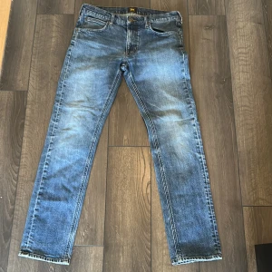 Blå Lee jeans straight fit - Säljer ett par klassiska blå jeans från Lee med raka ben och normal passform. Jeansen har fem fickor, snygg tvätt och tydliga slitningar för en cool look. Perfekta till vardags med t-shirt eller hoodie.