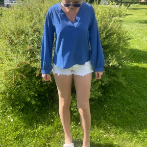 Blå långärmad blus med v-ringning - Snygg blå blus med v-ringad hals och långa ärmar. Modellen är rak och lite lösare i passformen, perfekt till jeans eller shorts. Tunt och luftigt tyg som passar bra till varmare dagar.