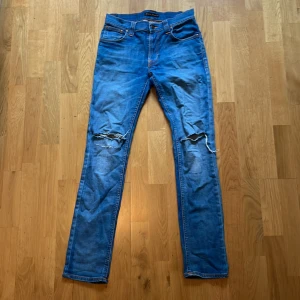 Ljusblå Nudie Jeans  - Säljer ett par ovanliga ljusblå jeans från Nudie Jeans med snygga slitningar och hål vid knäna. Modellen är Thin Tinn. Jeansen är i mjukt denimtyg och har detaljerade sömmar på bakfickorna. Storleken är 28/32. Köpt för 1200 säljer själv för 380