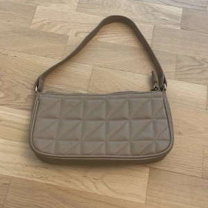 Beige väska ifrån Cubus (handväska/axelväska) - Snygg beige axelväska med quiltad framsida och guldfärgade detaljer. Väskan har en enkel, stilren form och dragkedja upptill. Insidan har ett fack med dragkedja för extra förvaring. Perfekt storlek för det viktigaste och passar till många outfits. Mycket modern väska och pris går att diskutera!👜