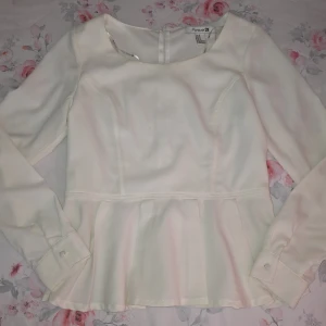 Vit blus med volang från Forever 21 - Supersöt vit blus från Forever 21 med långärmade ärmar och volang nedtill. Blusen har rund halsringning, markerad midja och dragkedja i ryggen. Perfekt för dig som gillar en feminin och stilren look.