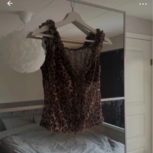 Leopardmönstrad volangtop - Snygg ärmlös topp med leopardmönster och volangdetaljer längs v-ringningen. Perfekt för dig som vill sticka ut och addera lite edge till outfiten. Toppen har en figurnära passform och är superenkel att styla med jeans eller kjol.