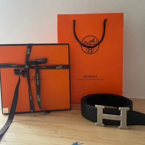 Svart bälte med H-spänne - Exklusivt svart bälte från Hemes med ikoniskt H-spänne i silverfärgad metall. Bältet är tillverkat i äkta skinn och levereras med originalförpackning, påse och certifikat. Perfekt accessoar för att lyfta vilken outfit som helst.
