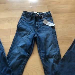 Molly high waist jeans blå S - Snygga Molly high waist jeans från Gina Tricot i klassisk blå tvätt. Modellen är högmidjad med smal passform och stretchigt jeanstyg. Perfekta basjeans med fem fickor och kopparfärgade detaljer. Storlek S.