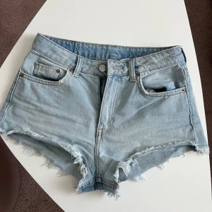 Ljusblå jeansshorts från H&M Divided - Snygga ljusblå jeansshorts från H&M Divided i storlek 36. Modellen är midwaist med klassisk femficksdesign och råa, fransiga kanter för en avslappnad vibe. Perfekta till sommaren och lätta att matcha med allt. Materialet är mjukt denim i bomull.
