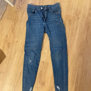 Blå skinny jeans från Jeanci, M - Snygga blå skinny jeans från Jeanci i stretchig bomullsblandning. Modellen har slitna detaljer på benen och råa, fransiga benslut för en trendig look. Klassisk femficksdesign och normalhög midja. Perfekta till sneakers eller boots.