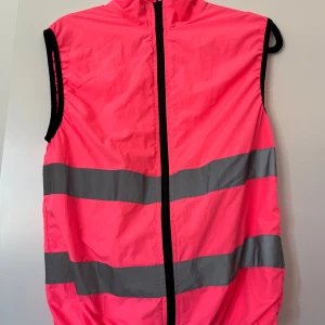 Neonrosa reflexväst med dragkedja - Neonrosa väst med två breda, reflekterande gråa band runt om och hel dragkedja framtill.