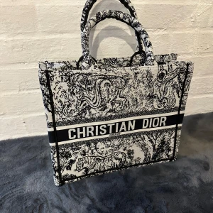 Christian Dior Book Tote handväska - Säljer en ikonisk Christian Dior Book Tote liknande handväska i svart och vitt med detaljerat djurmönster och tydlig logga framtill. Väskan har två rejäla handtag och är tillverkad i kraftig bomullscanvas. Perfekt för dig som vill sticka ut med en lyxig och trendig accessoar.