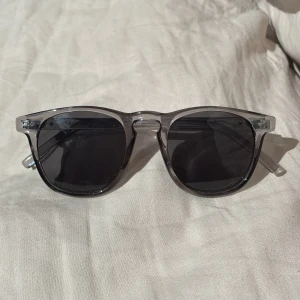 Svarta solglasögon med transparent båge - Snygga solglasögon med svarta glas och transparent grå båge. Klassisk, lite fyrkantig form som passar till de flesta stilar. Lätta och bekväma att bära, perfekta för soliga dagar.