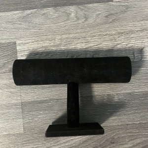 Svart smyckesställ i sammet - Snyggt svart smyckesställ i cylinderform, perfekt för att visa upp armband eller klockor. Stället är klätt i mjuk sammet och har en stadig fot. Passar perfekt på sminkbordet eller i garderoben för att hålla ordning på dina favoritsmycken.