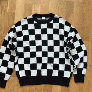 Svartvit rutig stickad tröja Lindex - Snygg stickad tröja från Lindex i storlek 146/152. Tröjan har ett coolt svartvitt rutigt mönster, rund halsringning och långa ärmar. Perfekt för dig som gillar streetstyle och vill sticka ut lite extra.