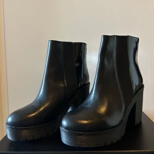 Svarta chelsea boots med klack från Henry Kole - Snygga svarta chelsea boots i skinn med chunky klack och plattformsula. Skorna har elastiska paneler på sidorna och grov räfflad sula för extra edge. Perfekta för dig som vill ha en stilren men ändå cool look.