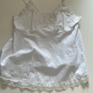 Vit linnetopp med spetsdetaljer - Supersöt vit linnetopp med tunna axelband och v-ringning. Toppen har fina spetsdetaljer längs urringning och nederkant. Perfekt att styla med jeans eller kjol för en fräsch look.💕