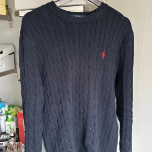 Mörkblå stickad tröja från Polo Ralph Lauren - Säljer en stilren mörkblå stickad tröja från Polo Ralph Lauren med det klassiska röda logotypen på bröstet. Tröjan har en rund halsringning och långa ärmar. Perfekt för kyligare dagar! Tröjan är tidigare från mitt äldre syskon som köpte den från nk.