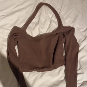 Brun ribbad offshoulder topp - Säljer en snygg brun ribbad offshoulder topp från SHEIN. Toppen har långa ärmar och en croppad passform, perfekt för en trendig look. Den unika designen med en axelrem ger en cool touch. Perfekt för att styla med jeans eller kjol!