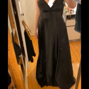 Svart långklänning med fin snörning i ryggen  - (Nypris 4000kr) (Helt ny oanvänd) Elegant svart långklänning med smala axelband och v-ringning. Klänningen har en snygg snörning i ryggen och passar perfekt till bal men även andra tillfällen. Står att storleken är 42, men jag är vanligtvis storlek 36/38 och denna klänningen passar perfekt på mig då den är liten i storleken och man kan justera storleken med snörningen i ryggen. Även ett perfekt alternativ för dig med större byst. (Prislapp kvar, kommer i orginalförpackning)