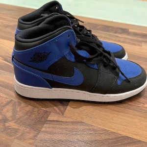 Nike Air Jordans i svart och blått - Använda 1 gång. Lite dammiga då dem bara stått och samlat damm, lätta att rengöra. Snygga Nike Air Jordans i en cool kombination av svart och blått. Skorna har en klassisk hög design med snörning och en vit sula som ger en sportig look. Perfekta för dig som vill ha stil och komfort i ett.