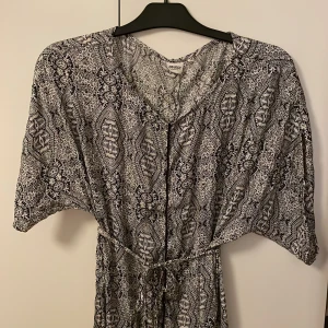 Mönstrad klänning från Object - Snygg mönstrad klänning från Object med ett snöre att knyta i midjan. Klänningen har korta ärmar och ett unikt mönster i svart och vitt. Perfekt för en stilfull look.