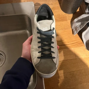 P448 sneakers - Snygga vita sneakers med svarta snören och detaljer. Skorna har en klassisk design med perforeringar på sidorna för extra stil. Perfekta för en avslappnad look.