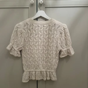 Vit stickad topp från Zara - Säljer en söt vit stickad topp från Zara med korta ärmar och volangdetaljer vid ärmslut och nederkant. 