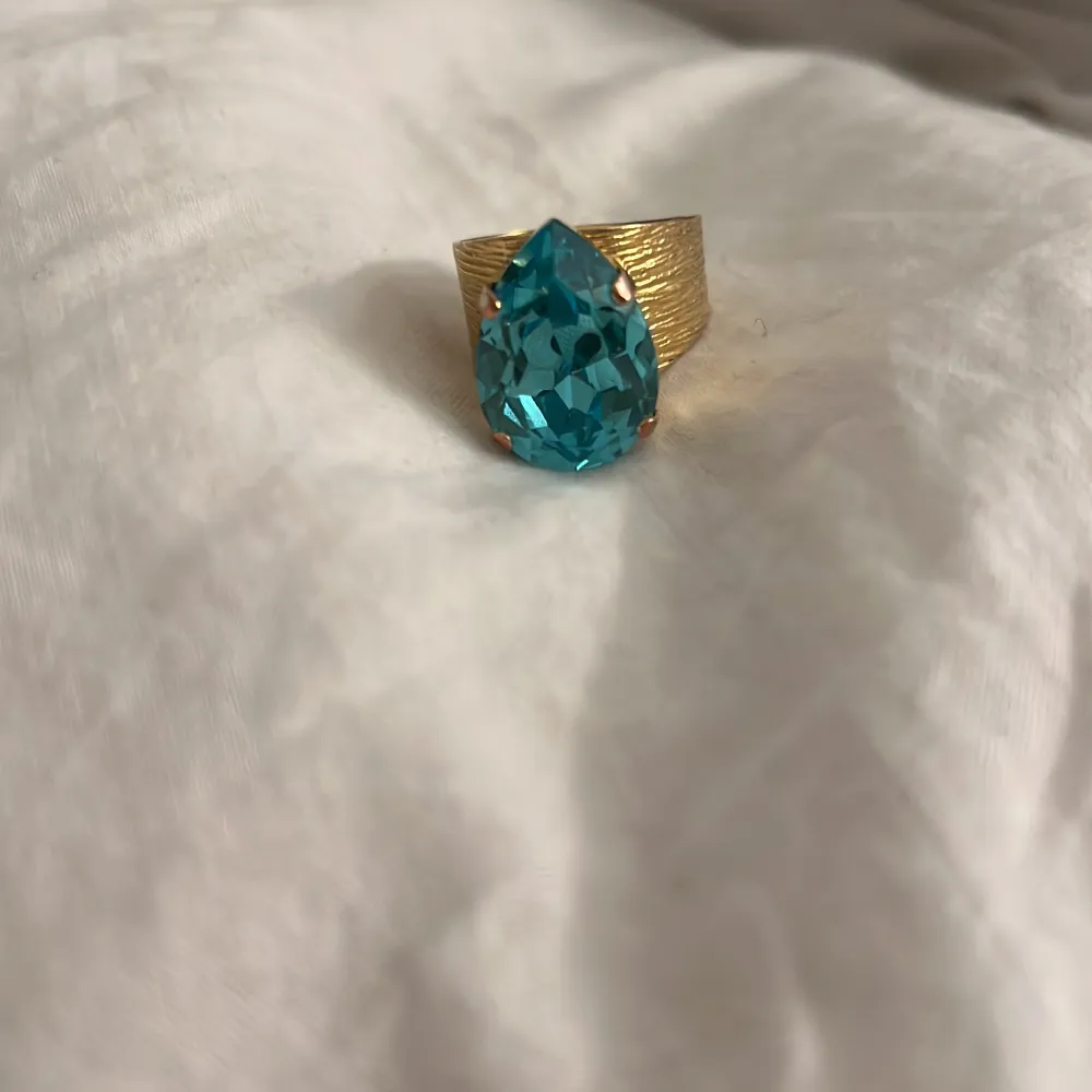 Snygg guldfärgad ring från Caroline Svedblom med en stor, droppformad sten i aquamarine. Säljer då jag har två nu.. Asusteet.