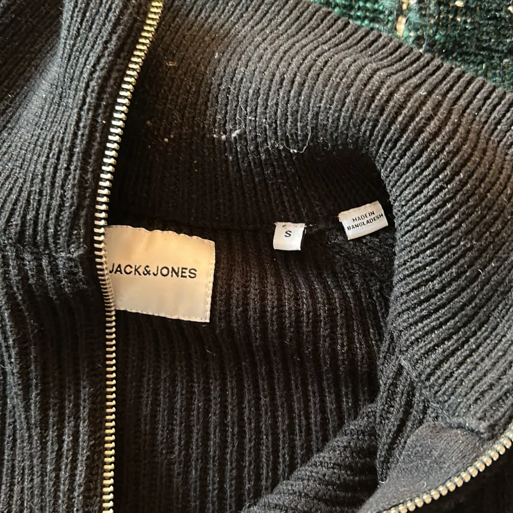 Säljer en stilren svart ribbad tröja från Jack & Jones med dragkedja i halsen. Perfekt för kyligare dagar med sin långa ärmar och bekväma passform. Ett måste i garderoben för en klassisk look.. Neuletakit & Villapaidat.