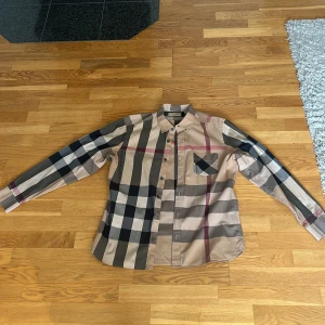 Rutig skjorta från Burberry - Säljer en i princip oanvänd stilren rutig skjorta från Burberry.Skjortan har långa ärmar och en klassisk krage med knappar framtill. Storlek L men sitter  som en M.     Priset går att diskuteras vid snabb affär 