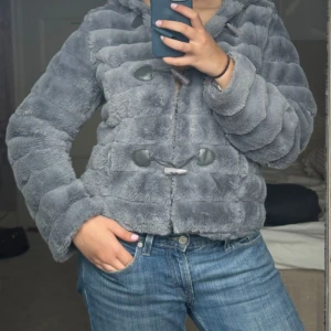 Grå pälsjacka med huva - Säljer en mysig grå pälsjacka från Angela Davis i storlek M. Jackan har en huva och stängs med knappar. Jag har vanligtvis M-L  i jackor och är 170 för referens :) Perfekt skick och så skön