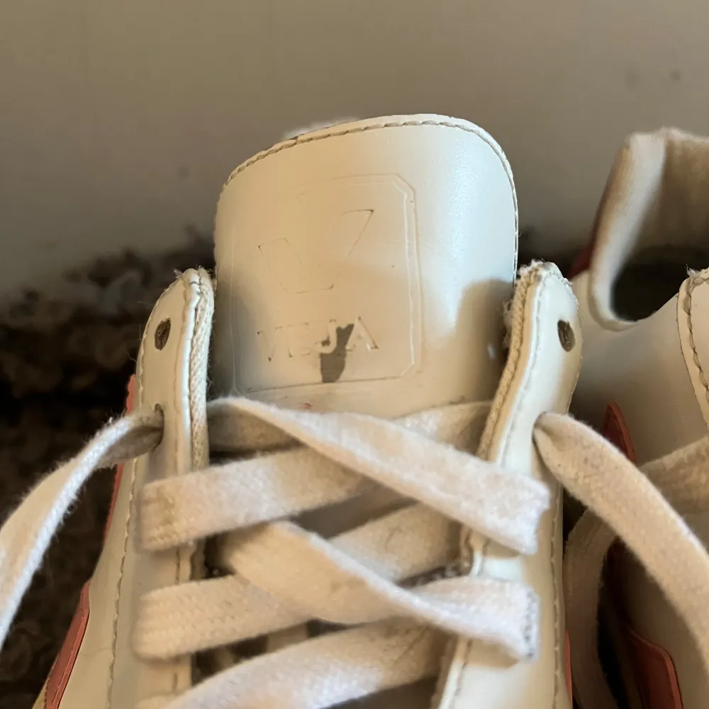Säljer ett par stilrena vita sneakers från Veja med rosa V-logga på sidan och vinröd häl. Skorna har snörning och en bekväm sula, perfekt för en avslappnad stil. Små deffekter på skorna . Kengät.