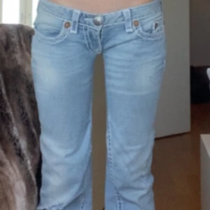 Ljusblå true religion jeans - Snygga ljusblå jeans från True Religion med broderade detaljer på bakfickorna. De har en låg midja och en straight/ bootcut passform. De är omsydda så att de ska vara mer lågmidjade.                                                  Midja: 36cm Innerbenslängd: 77cm Grenhöjd: 15cm