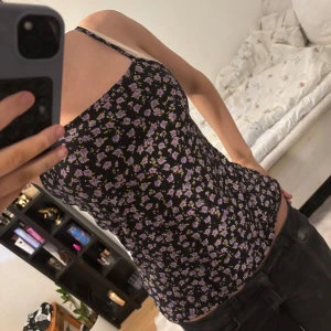 Blommig linnetopp - Säljer en söt blommig linnetopp med smala axelband. Toppen har en svart bas med lila och gula blommor, perfekt för en somrig look. Den är figurnära och passar bra till både jeans och kjol. Perfekt för varma dagar eller som ett lager under en kofta. Skulle säga att den nog är S men det står inte💞
