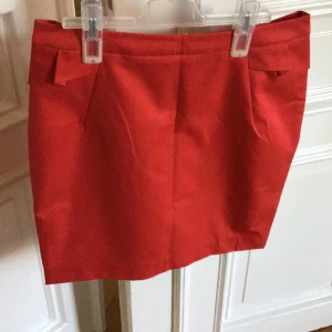 Röd kjol med dragkedja - Snygg röd kortkjol från H&M med dragkedja bak. Perfekt för att ge en färgklick till din outfit. Kjolen har en stilren design med diskreta detaljer vid midjan. Strl 40.