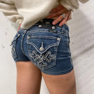 Blå jeansshorts från Miss Me - Snygga blå jeansshorts från Miss Me med dekorativa broderier och pärlor på bakfickorna. Shortsen har en tajt låg midjad passform perfekt för sommarn😊