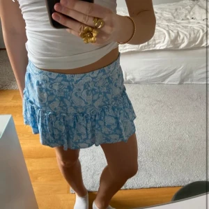 Zara kjol - Säljer en söt blå kortkjol med vitt paisleymönster. Kjolen har volangdetaljer och ett knytband i midjan för justerbar passform. Även inbyggda shorts (se bild 4) Perfekt för varma sommardagar!