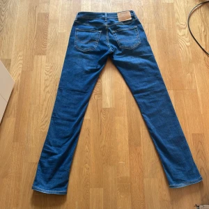 Blå jeans från Jack & Jones - Snygga blå jeans från Jack & Jones med klassisk femficksdesign och knappgylf. Perfekta för en avslappnad stil. Märkeslogga på insidan av linningen och subtila sömdetaljer på bakfickorna. Priset är inte hugget i sten!!