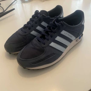Adidas L.A. Trainer sneakers - Snygga Adidas L.A. Trainer sneakers i marinblått med vita detaljer och klassiska tre ränder. Skorna har en retro look med snörning och en unik sula med gummiknoppar för extra grepp. Storleken är 43 1/3 o är i mycket bra skick