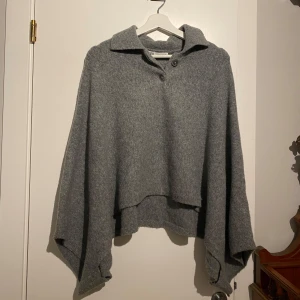 Stickad poncho från Zara! Ny och oanvänd!  - Snygg och bekväm grå poncho från Zara med krage och knappar framtill. Perfekt för lager-på-lager under kyliga dagar. Den har en lös passform och är tillverkad i ett mjukt material. Tyvärr är prislappar borttagna då det var en present, men den är aldrig använd! 