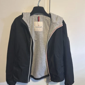 Svart windbreaker jacka från Moncler - Säljer en super fet windbreaker jacka från moncler som jag köpte på NK för 1 år sen. Väldigt bra skicke och använts sparsamt. Finns en tag inuti jacka som visar att den är äkta här samt lite extra jag fick med som knappar och en triangel sak. Är size 12A och passar max till de som är 158 innan den blir för tight. PRISET ÄR EJ HUGGET I STEN