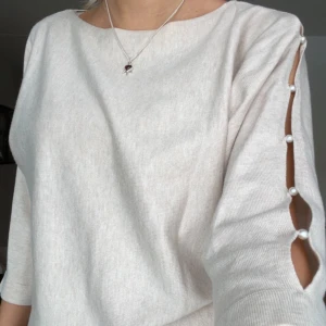 Beige tröja med pärldetaljer - Säljer en stilren beige tröja med unika pärldetaljer längs ärmarna. Tröjan har trekvartsärm och en mjuk, bekväm passform. Perfekt för en elegant vardagslook.