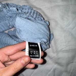 Blå ribbad topp från Shein - Säljer en blå ribbad topp från Shein med knappar framtill och volangdetaljer längs kanterna.