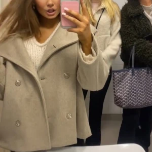 Beige kappa med knappar - Snygg beige kappa med bred krage och dubbelknäppning. Perfekt för kyligare dagar med sin stilrena design och långa ärmar. Super fint skick.