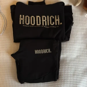 Svart hoodie och byxor från Hoodrich - Säljer en svart hoodie och matchande byxor från Hoodrich. Hoodien har en stor logga framtill och en praktisk magficka. Byxorna har en mindre logga på benet och elastisk midja för bekväm passform. Perfekt set för en avslappnad stil.