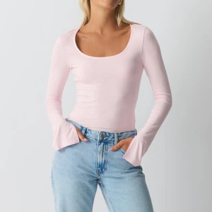 Ljusrosa långärmad topp - Säljer en ljusrosa långärmad topp med en rundad halsringning. Toppen har en tight passform och är tillverkad i ett mjukt material. Ärmarna har en lätt utsvängd design som ger en unik touch. Perfekt för att styla med jeans eller kjol.