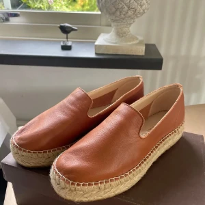 Bruna skinn espadrillos från Macarena 37  - Snygga bruna espadrillos från spanska Macarena i  mjukaste skinn med en klassisk flätad sula. Perfekta för en avslappnad stil och handgjorda för extra kvalitet. De har en enkel slip-on design som gör dem lätta att bära. Handgjorda , original kartong. Fin cognac färg.